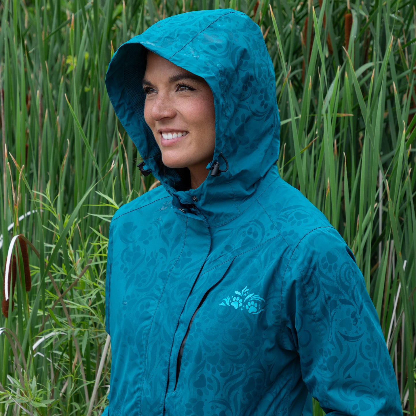 Person wearing a blue raincoat with the hood pulled up, standing in tall green grass.
