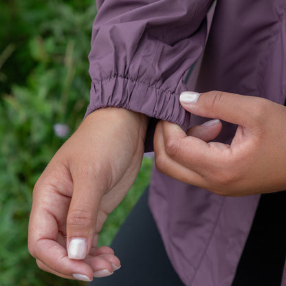 Close-up of a hand adjusting the sleeve of a purple rain jacket with a blurred green background outdoors.