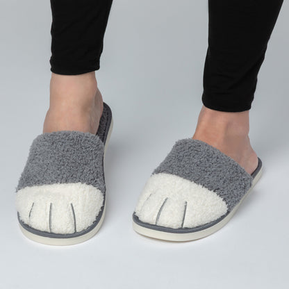 Gray fuzzy slippers with white soles worn by a person on a light gray background