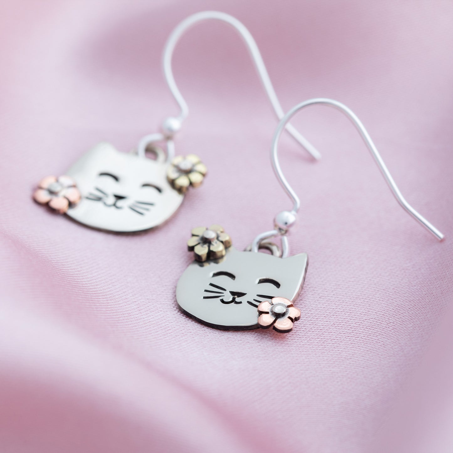 Cat-shaped earrings with floral details on a pink background