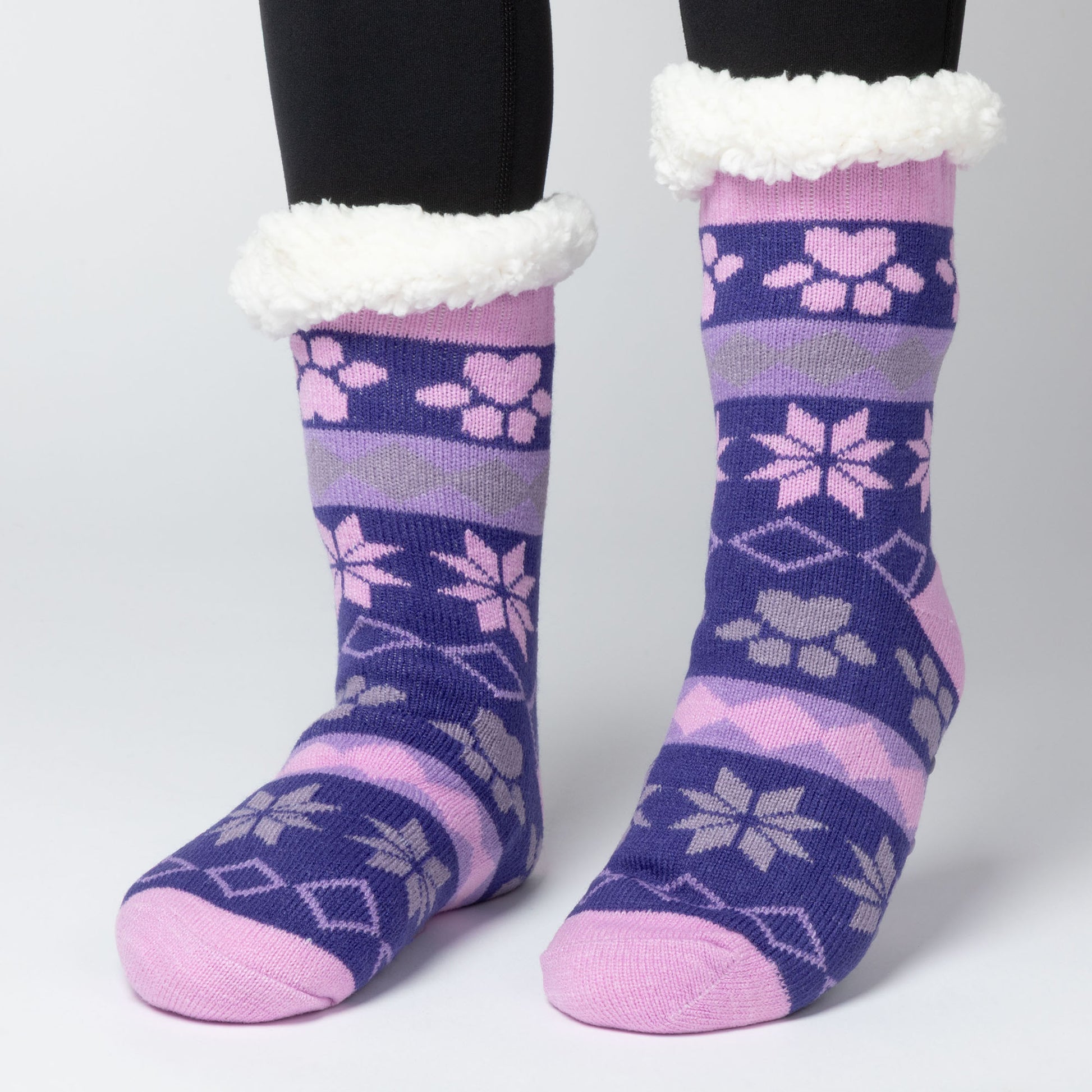 model wearing Pair of pink, gray purple Sherpa Fleece Lined Paw Print Cabin Slipper Socks with sherpa trim on a light gray background alpine fair isle paws plum