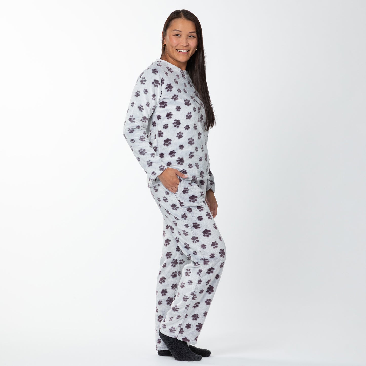 A woman wearing a matching set of fluffy, soft long-sleeve pajamas. The top and pants are light grey and patterned with purple paw prints. Her hand is in one of the two usable pockets. 