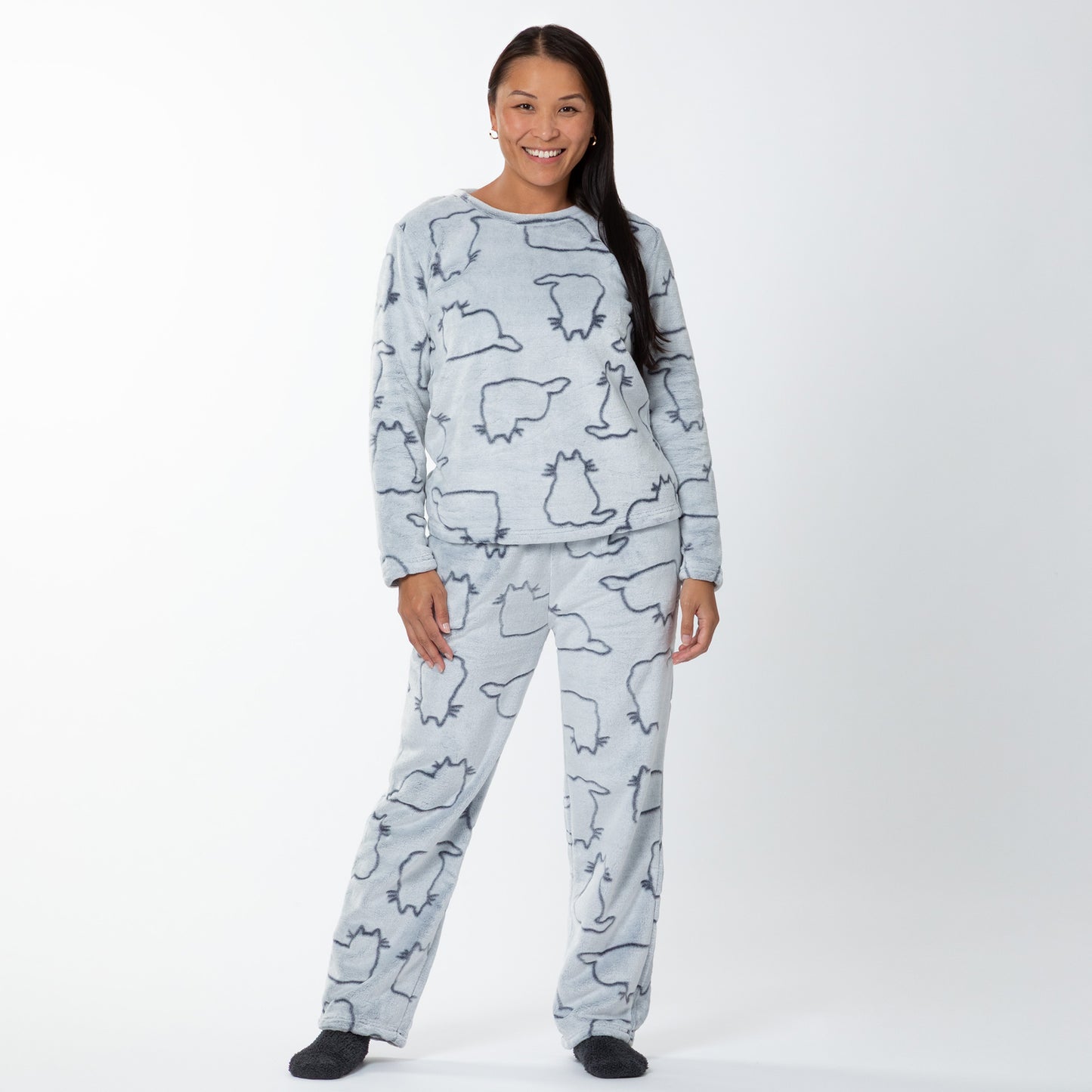 A woman wearing a matching set of fluffy, soft long-sleeve pajamas. The top and pants are light grey and patterned with cute cat outlines. 