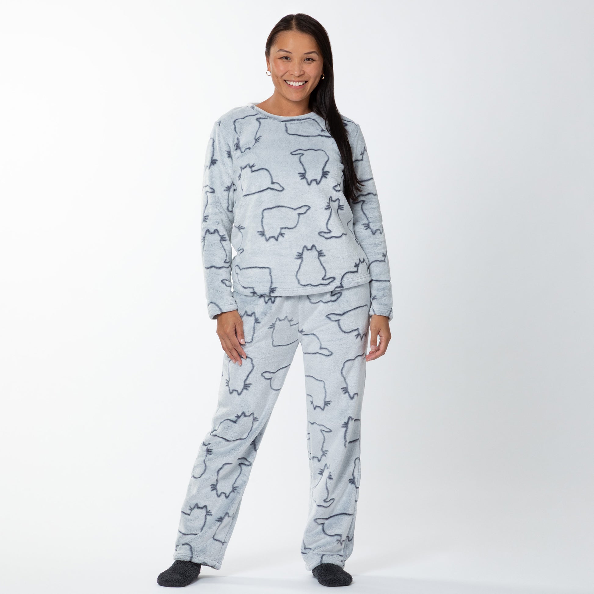 A woman wearing a matching set of fluffy, soft long-sleeve pajamas. The top and pants are light grey and patterned with cute cat outlines. 
