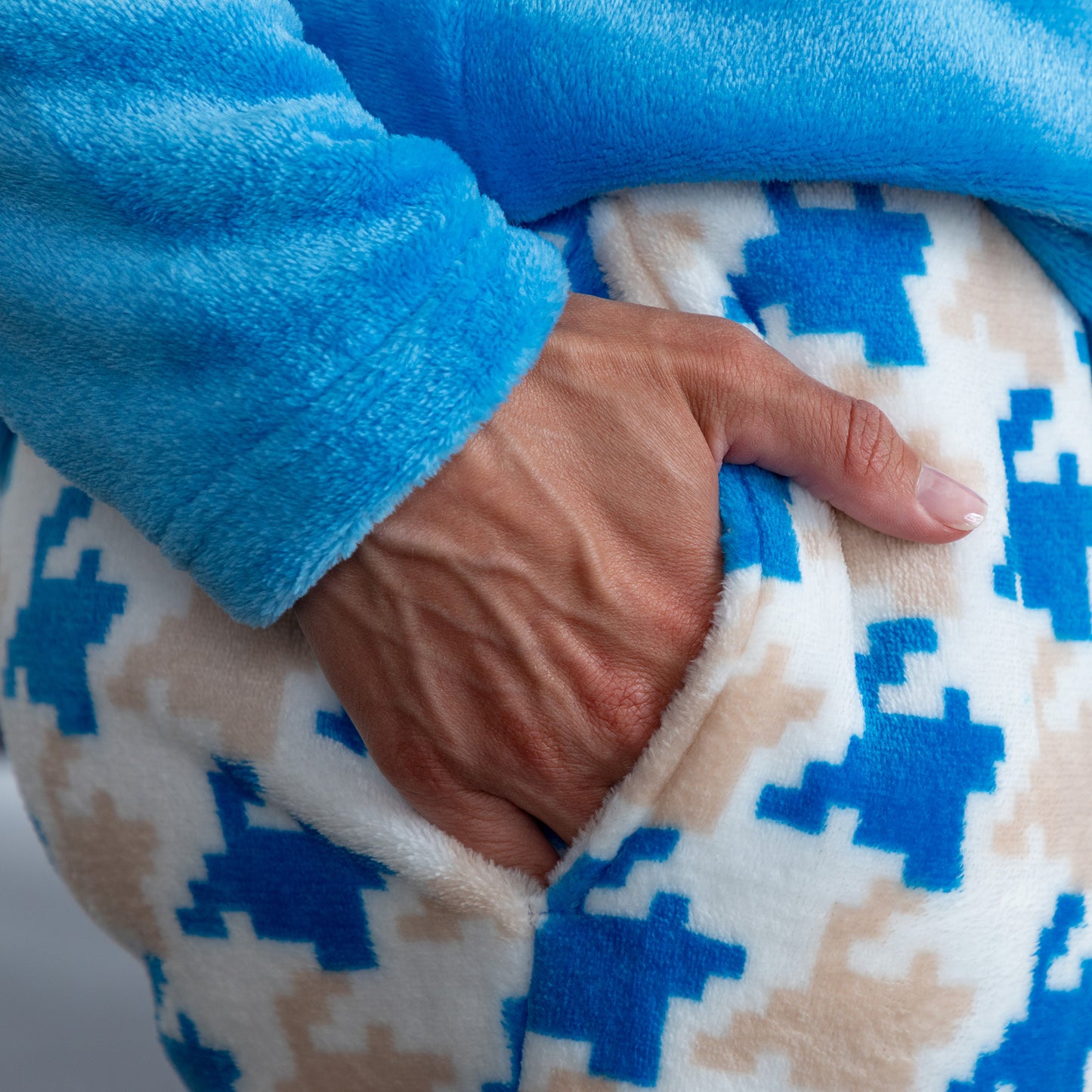 A detail image of a woman wearing a blue long-sleeve top with an embroidered cute cat design and gray, blue and light blue houndstooth pattern. Design a blue cat in super cozy fabric, showing model's hand in pocket 