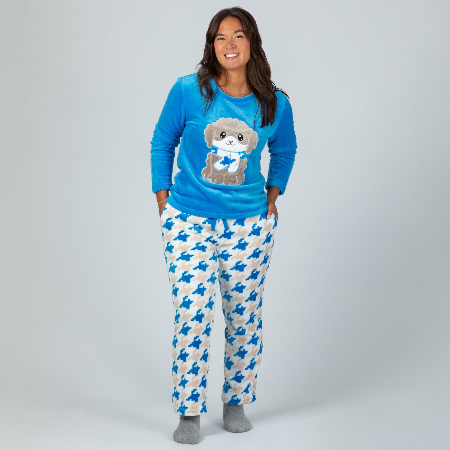 A woman wearing a blue long-sleeve top with an embroidered cute dog design and gray, blue and light blue houndstooth pattern. Design a grey dog with a scarf in super cozy fabric.