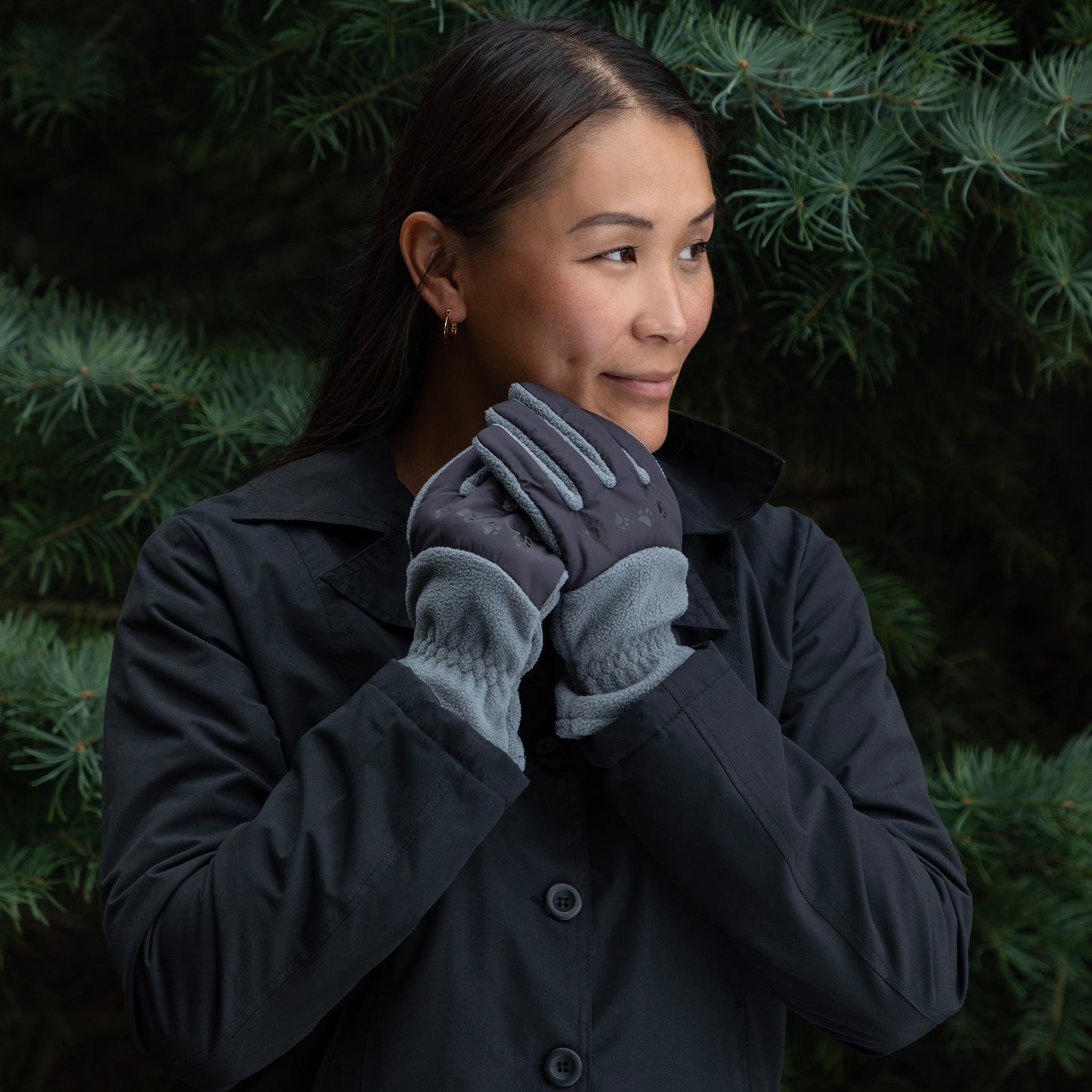 Woman wearing a dark coat and gray gloves against a green foliage background