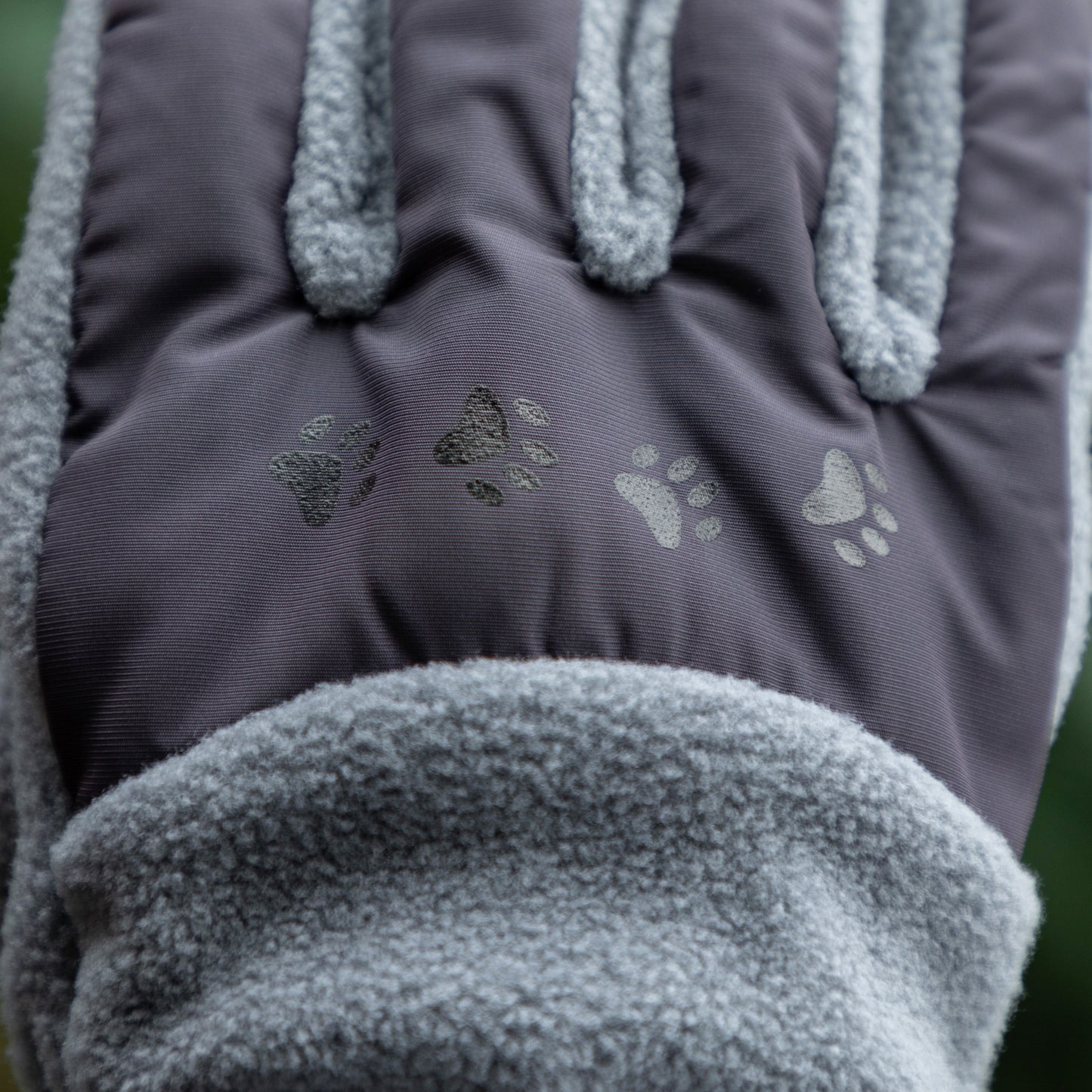 Close-up of a pair of gray gloves with paw print designs on a blurred green background
