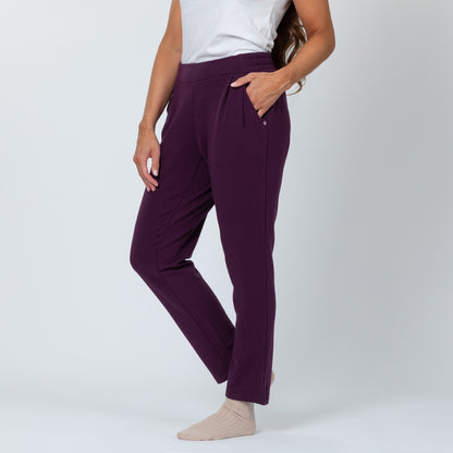 Person wearing purple pants and a white top on a plain background