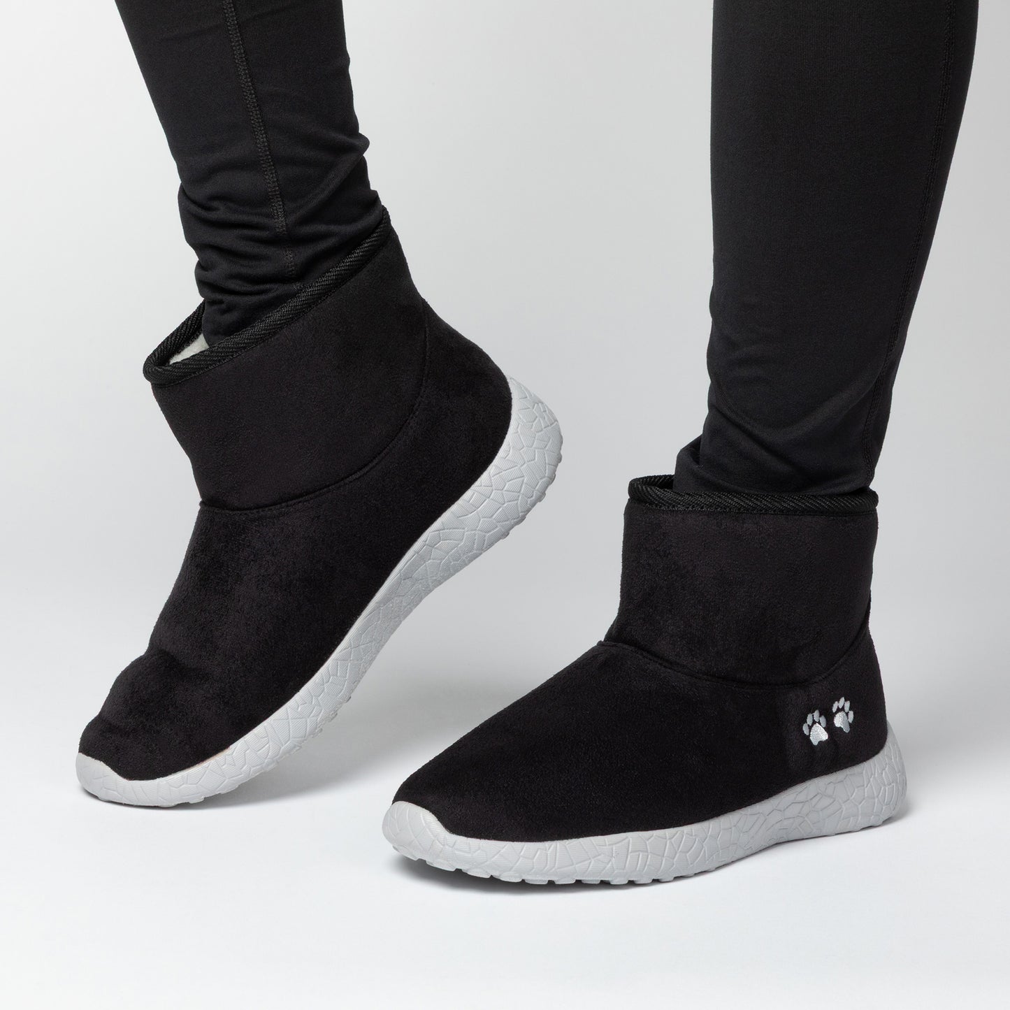 Black slip-on boots with white soles worn by a person on a light gray background