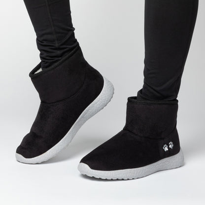 Black slip-on boots with white soles worn by a person on a light gray background