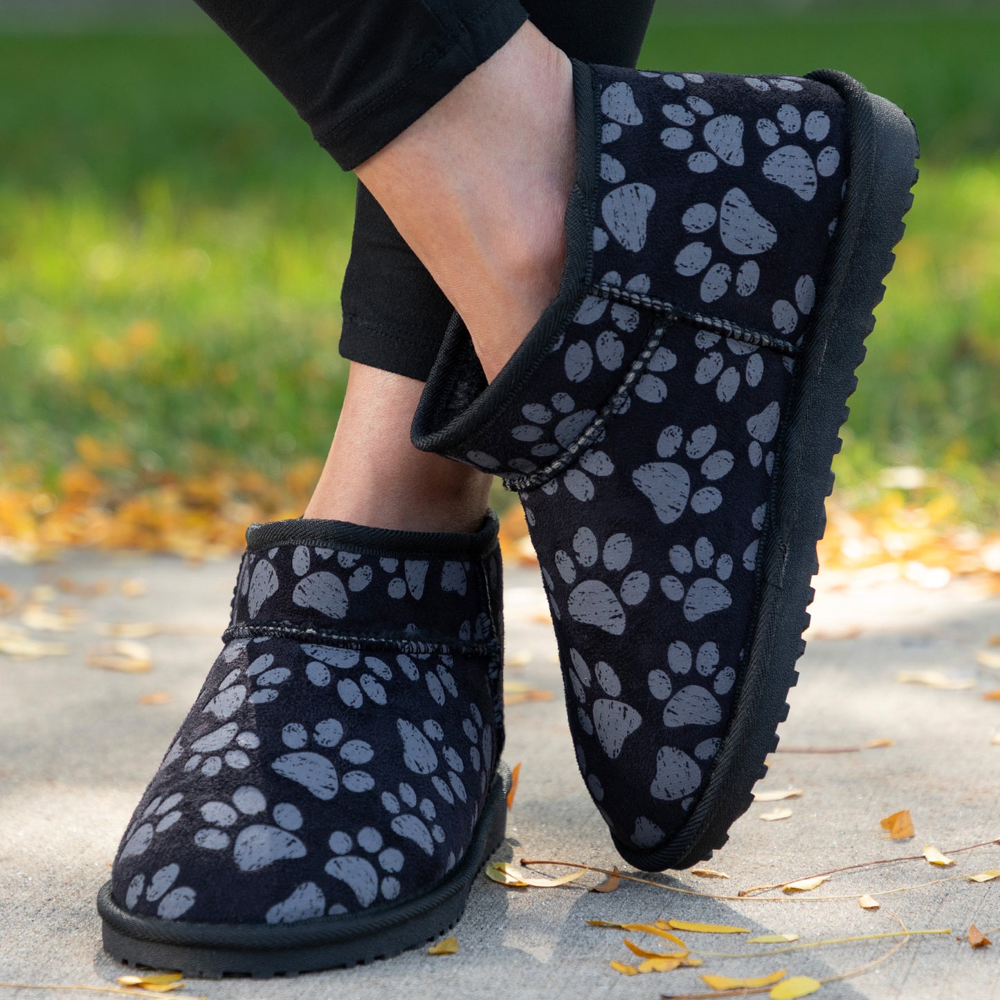 Black ankle boots with paw prints worn on a concrete surface with grass and leaves in the background