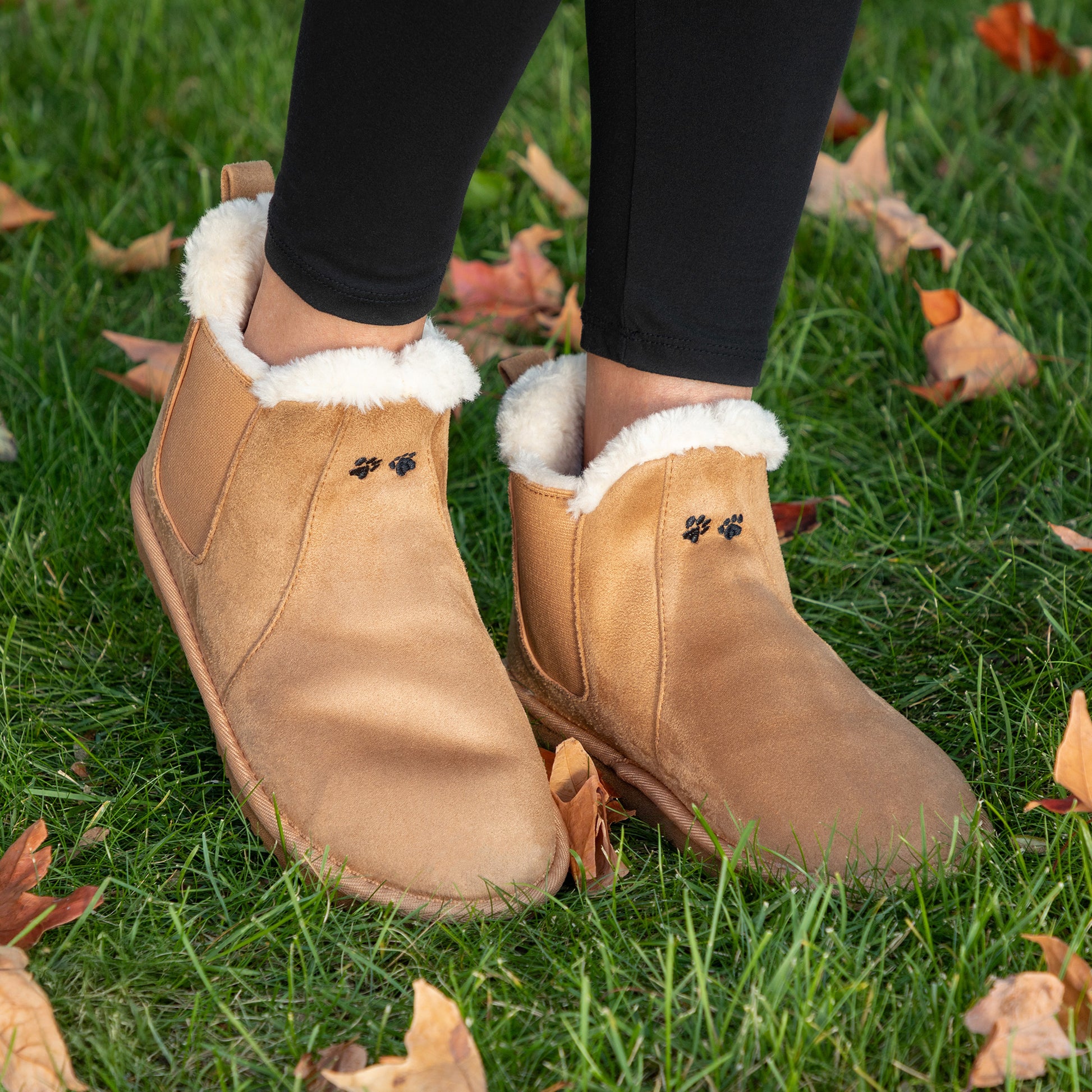 Tan suede boots with white fur lining worn on grass with fallen leaves.