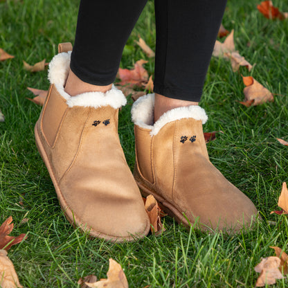 Tan suede boots with white fur lining worn on grass with fallen leaves.