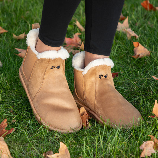 Tan suede boots with white fur lining worn on grass with fallen leaves.