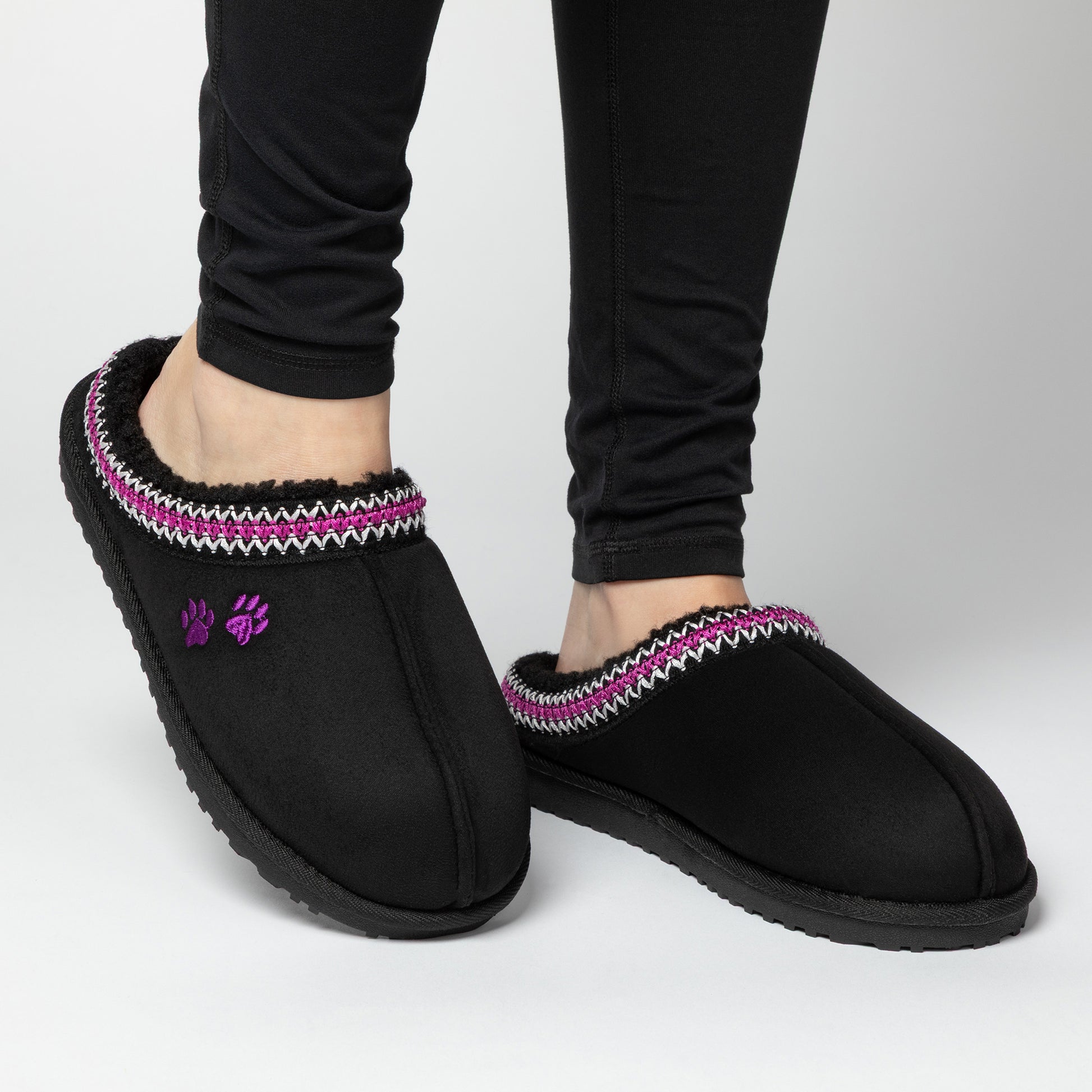 Black slipper shoes with purple and white trim worn by a person on a light gray background.