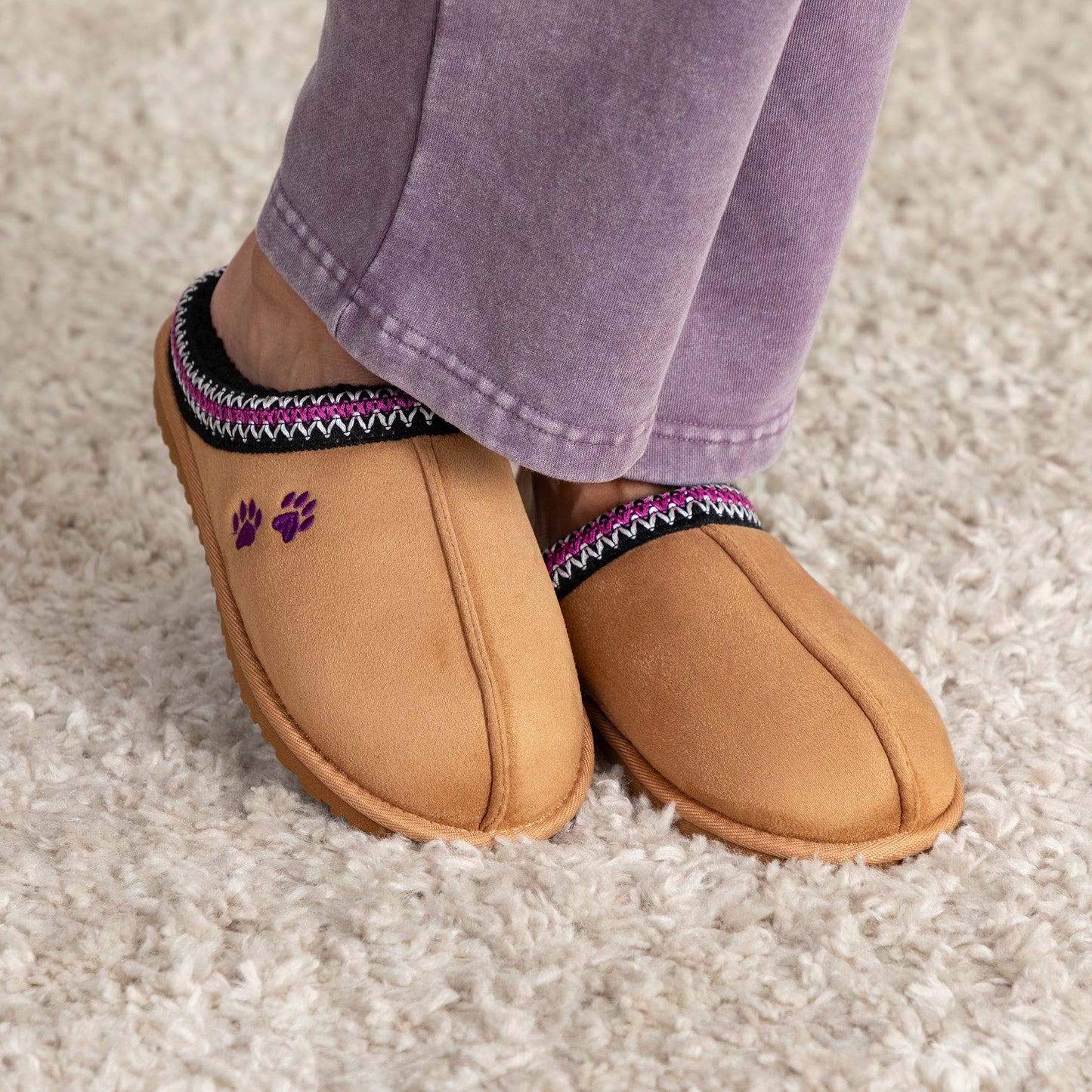 Tan slippers with paw prints and decorative accents around cuffs worn on a carpeted floor.