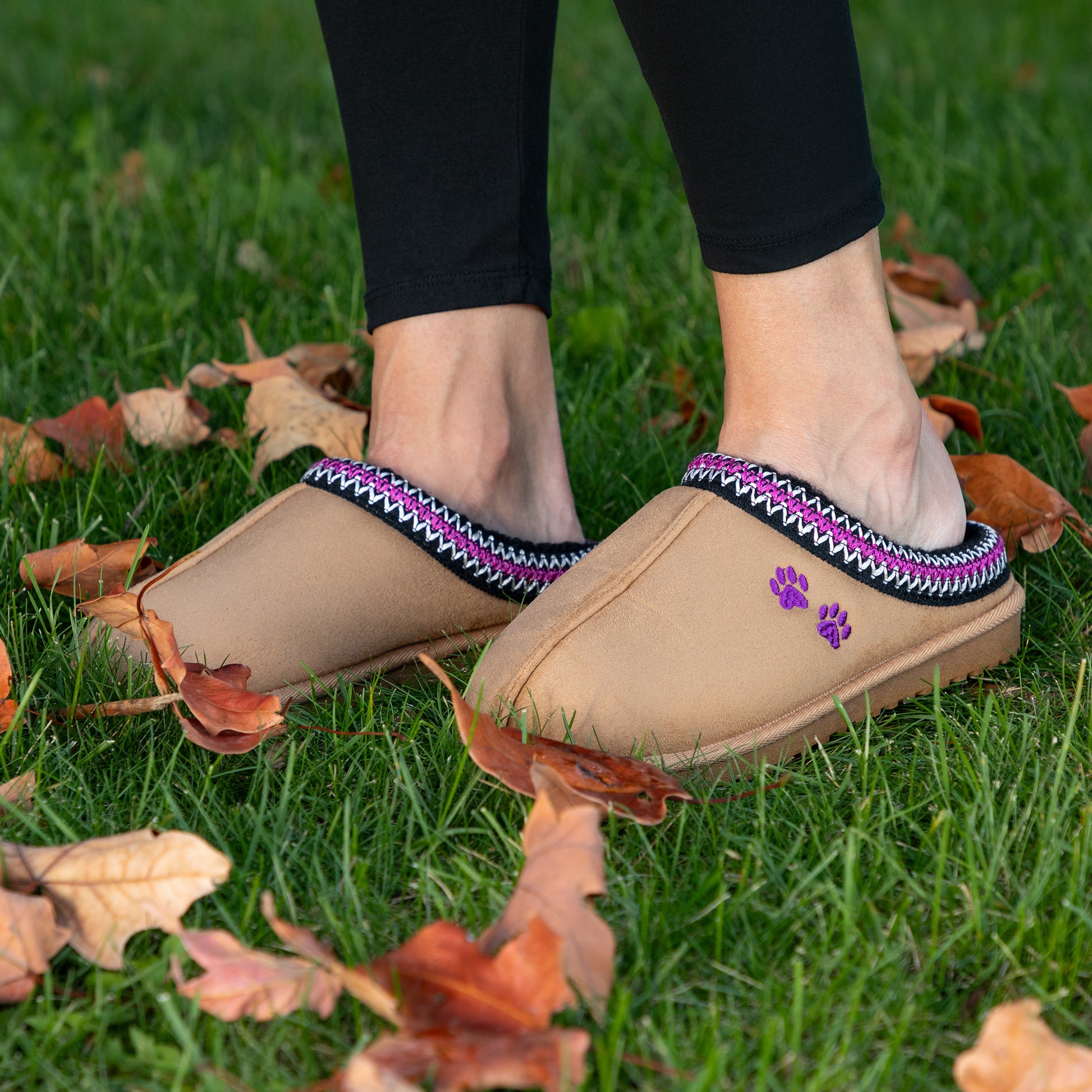 Beige slip on clogs with purple and black accents worn on grass with leaves