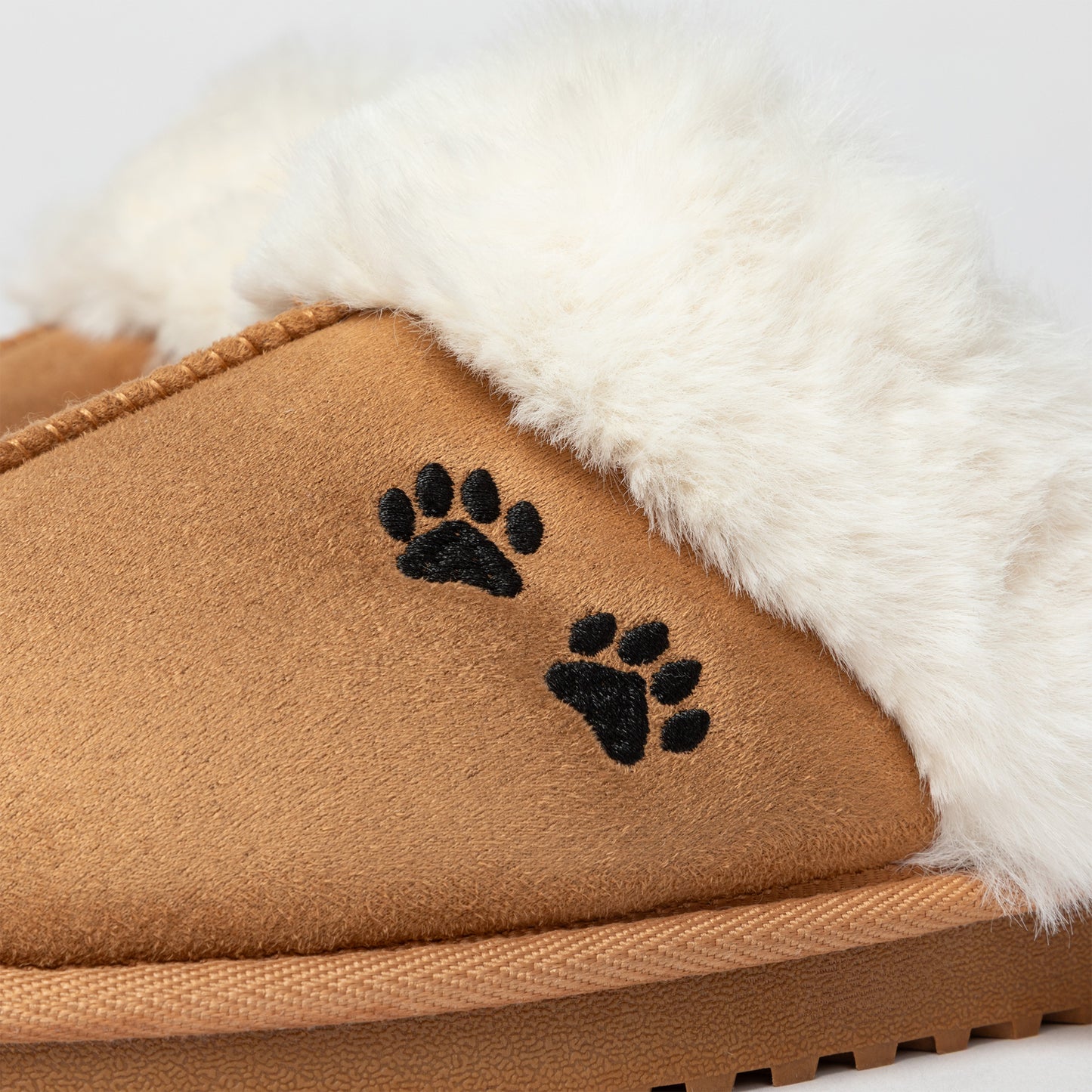 Tan slipper with white fur lining and black paw prints on a light gray background