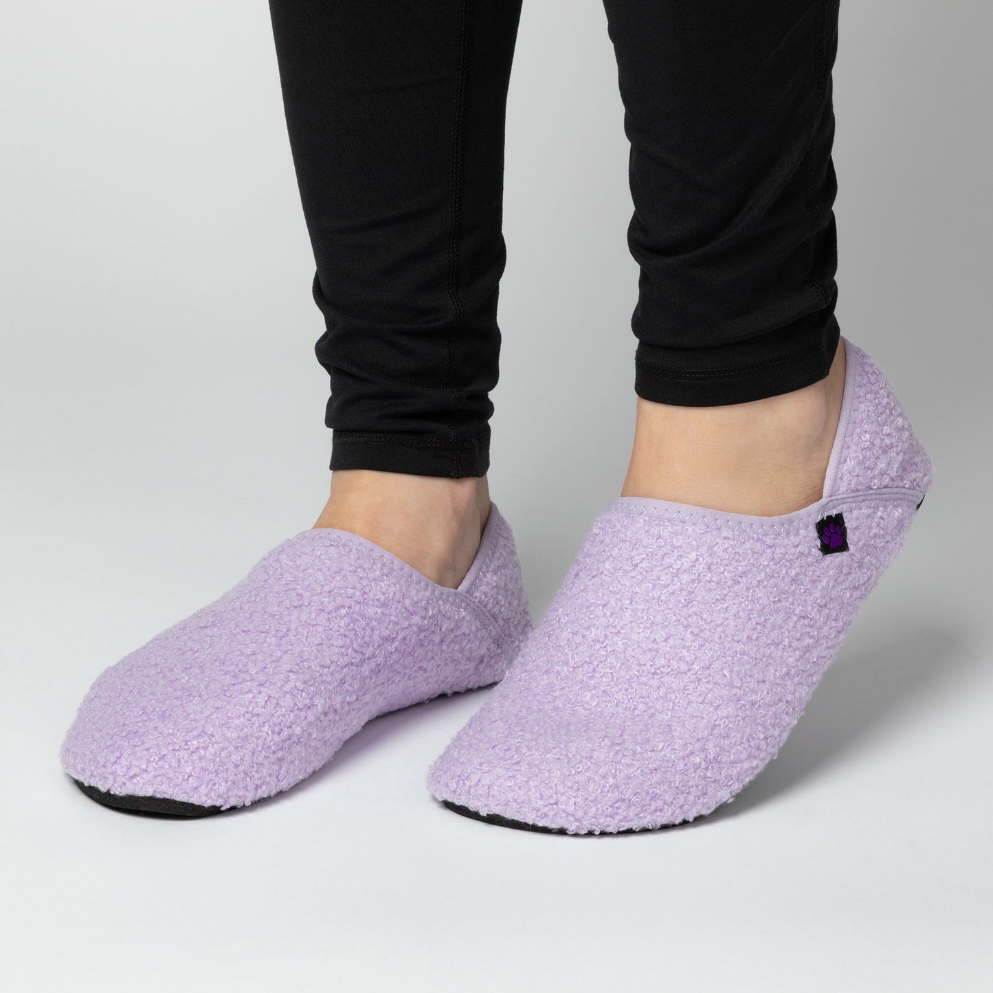 Purple slippers worn with black pants on a neutral background