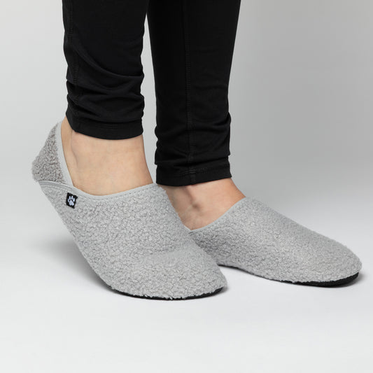 Gray slip-on shoes worn with black pants on a light gray background