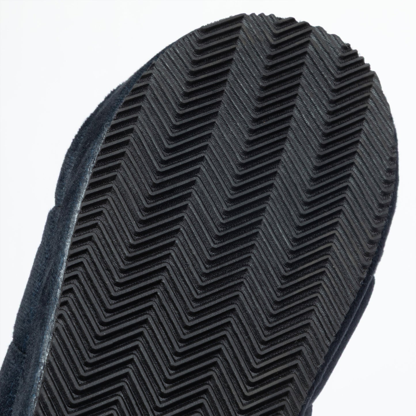Close-up of a black textured rubber sole with a herringbone tread pattern, set against a plain white background.