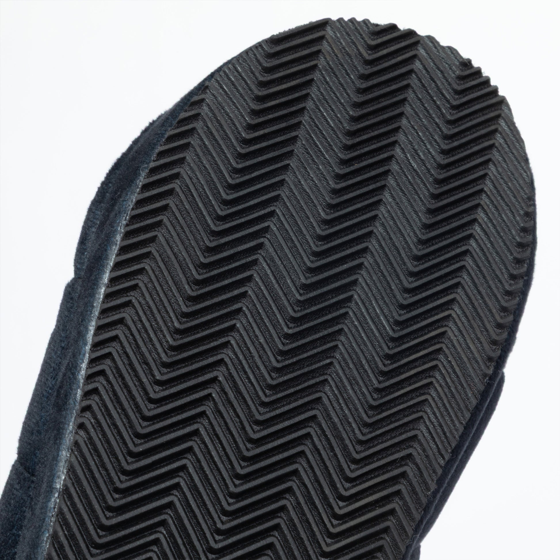 Close-up of a black textured rubber sole with a herringbone tread pattern, set against a plain white background.