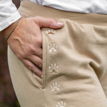 Tan pants with paw print design , hand in pocket, with a blurred background.