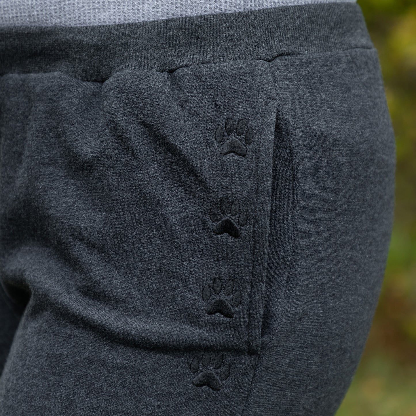 Dark gray pants with paw print design on a blurred green background