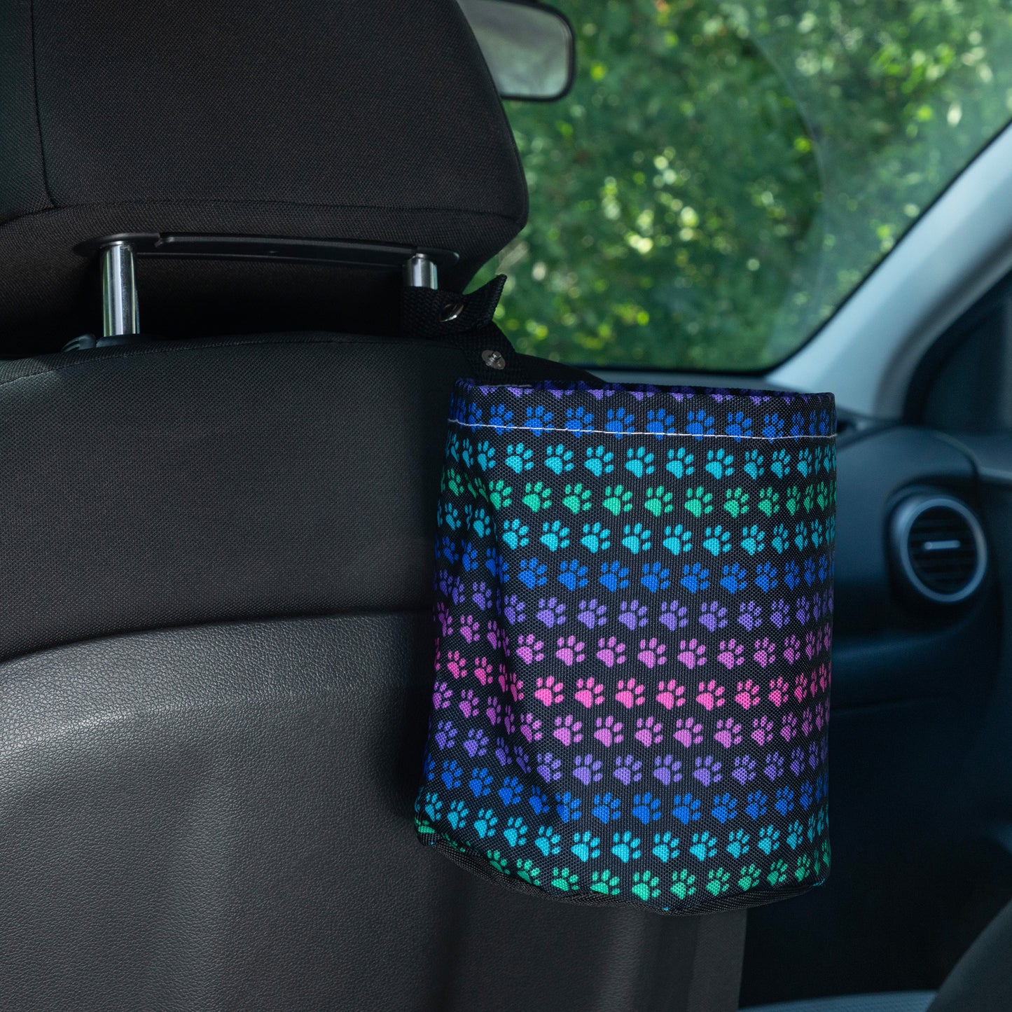 Car garbage holder cover with rainbow paw pattern in a car interior hanging on the headrest of the front seat. 