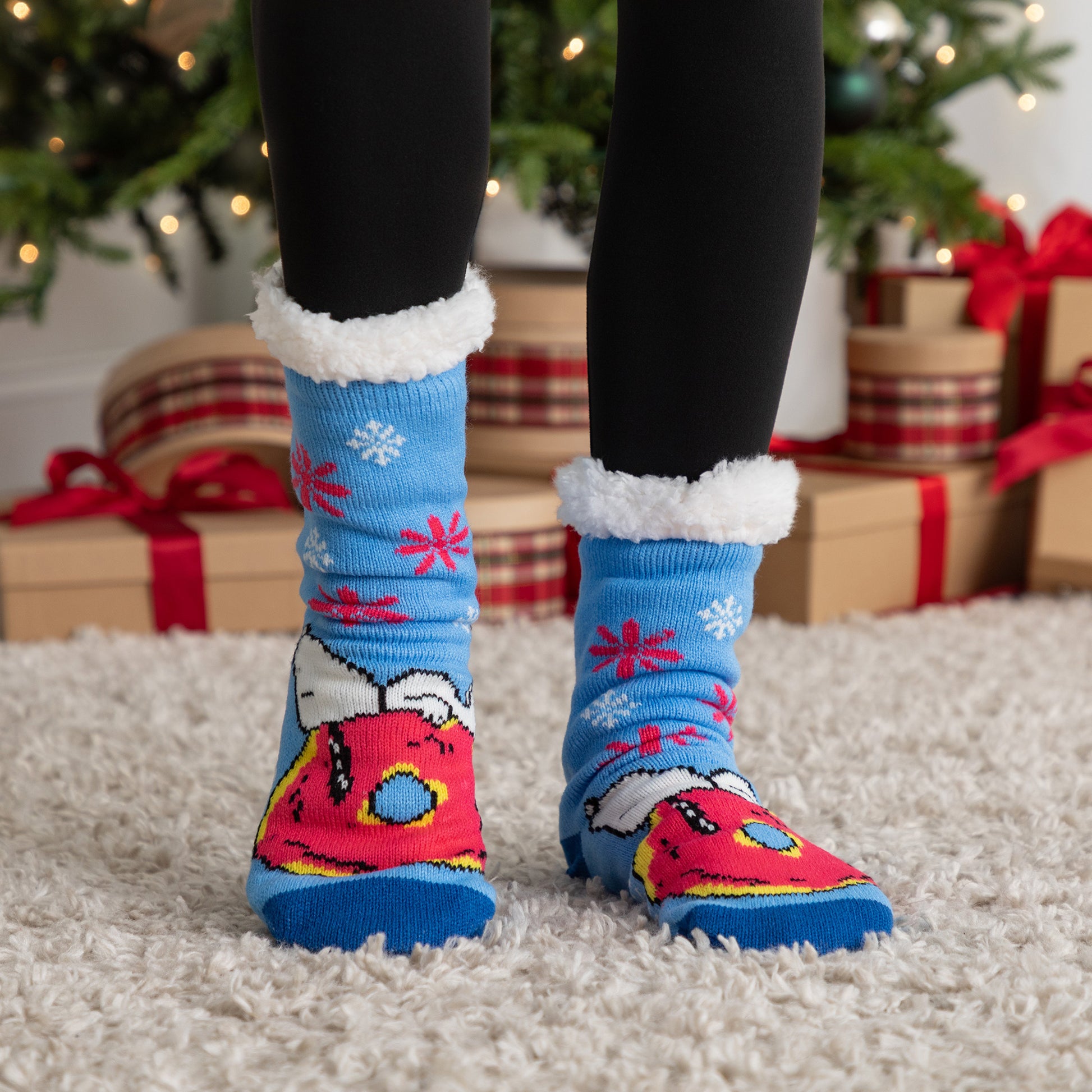 Colorful Christmas-themed socks with paw prints worn indoors, with a decorated Christmas tree and presents in the background.
