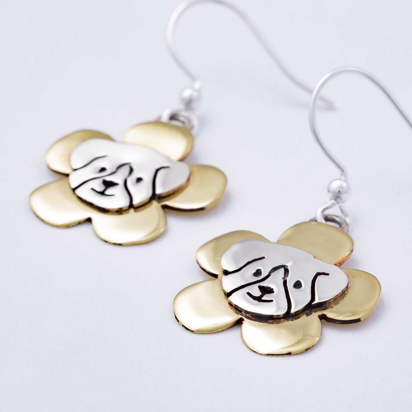 Brass and silver flower-shaped earrings with a dog face in the middle, on a white background