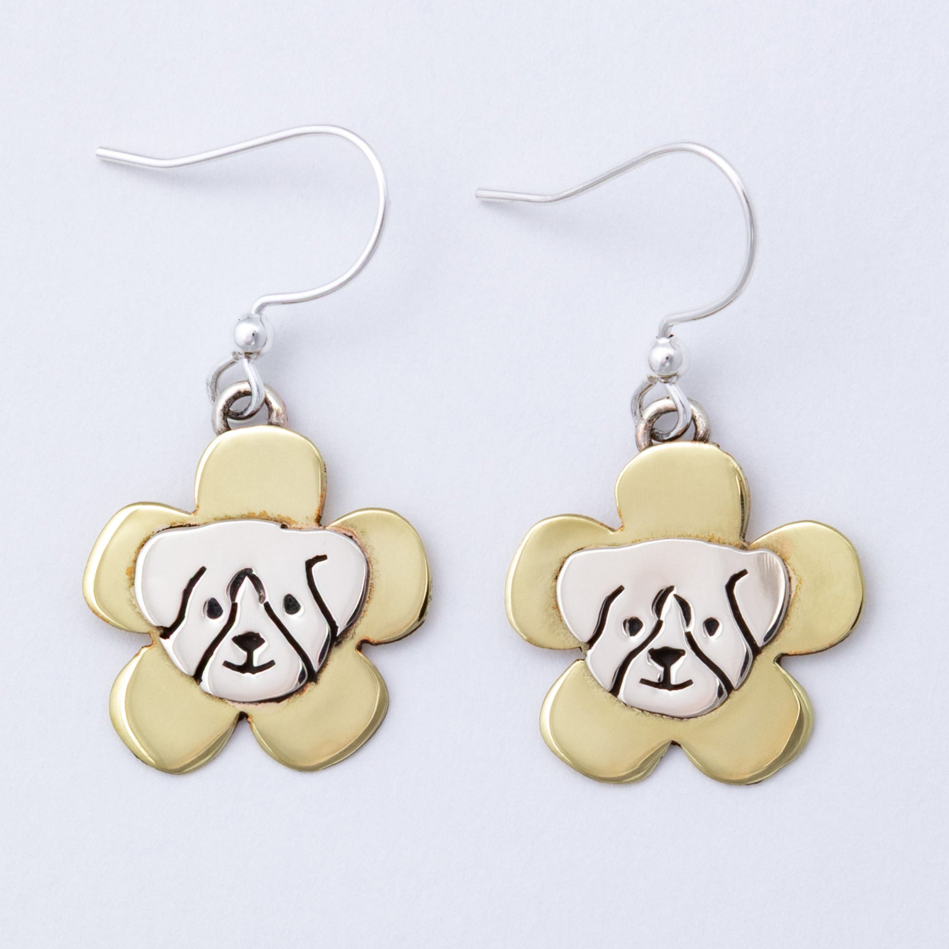Pair of earrings with dog face design on brass flower-shaped pendants against a white background