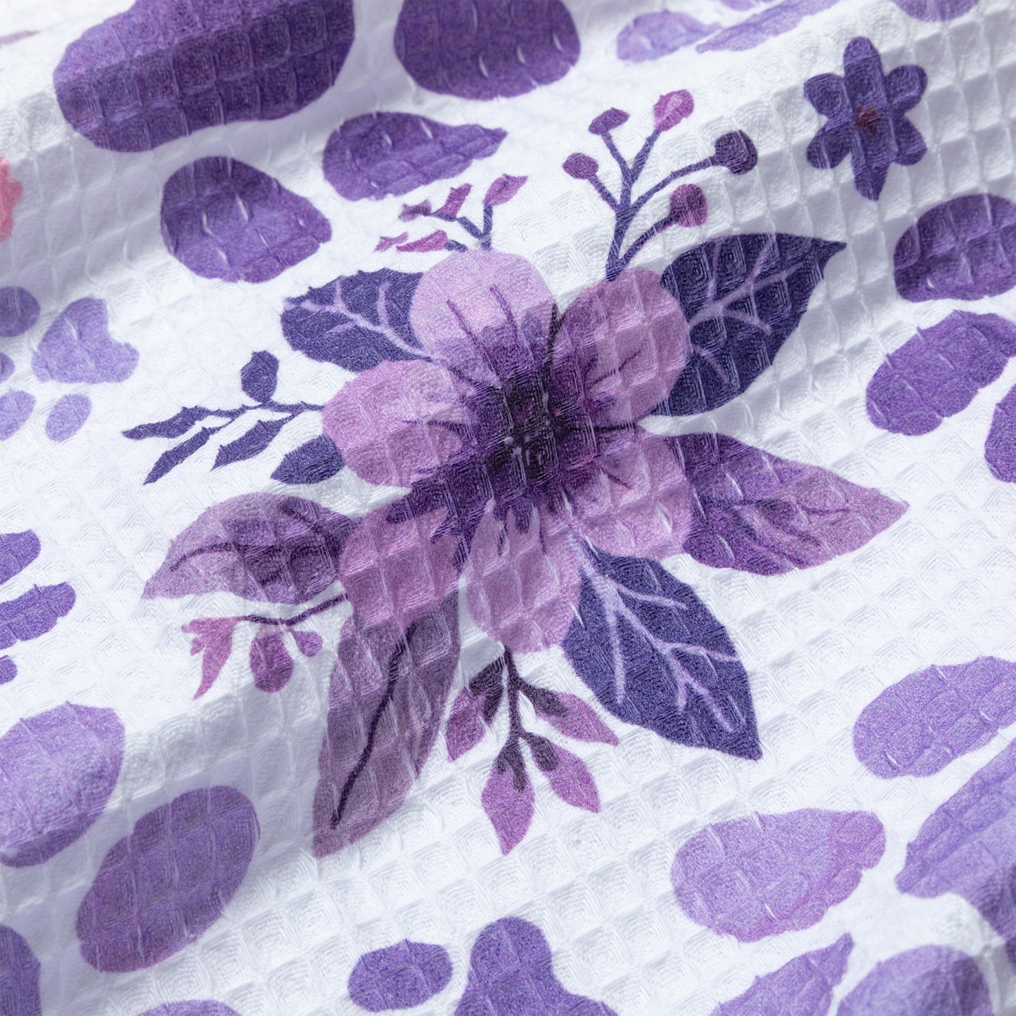 Close-up of a dish towel with purple floral design on a textured white background
