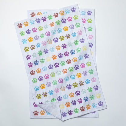 Two flat dish towels  patterned with colorful paw prints on a white background