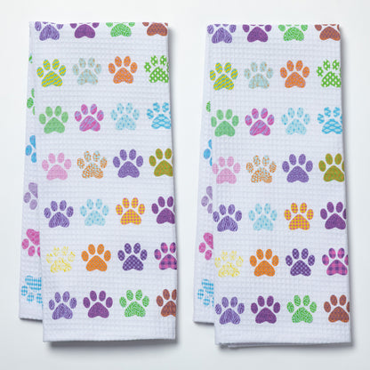 Two white dish towels with colorful paw print patterns on a white background