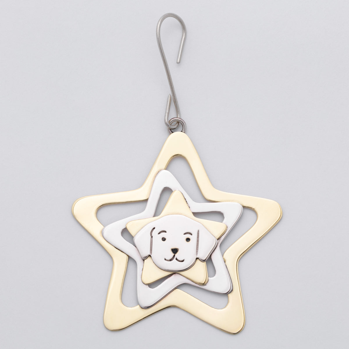 A metal ornament shaped like a star, featuring concentric star layers in gold, silver, and white, with a small white dog face charm in the center, shown on a light gray background.