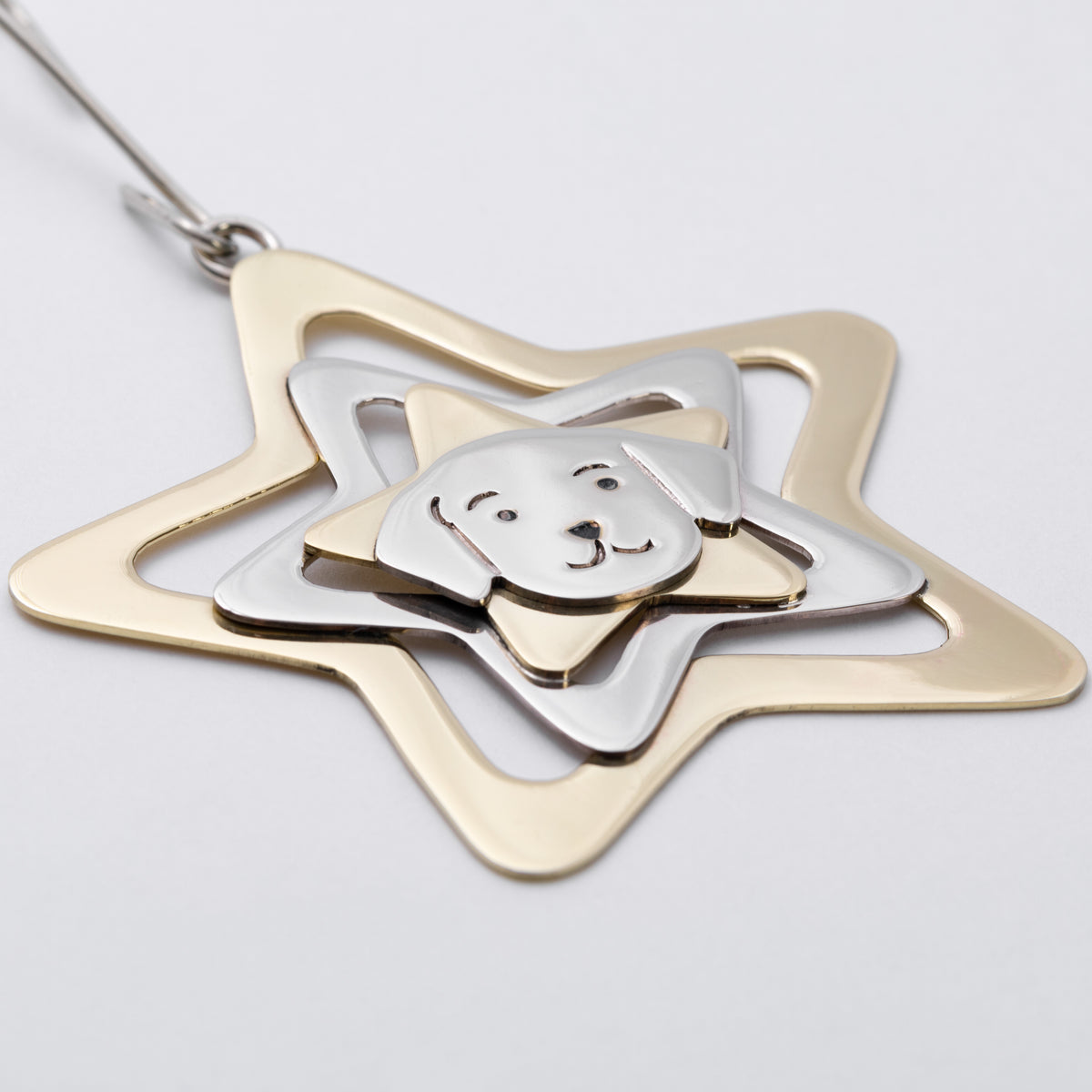 A two-tone metal pendant featuring a gold star-shaped frame with a silver inner star, dog head silhouette, and a silver chain loop at the top, shown on a light gray background.