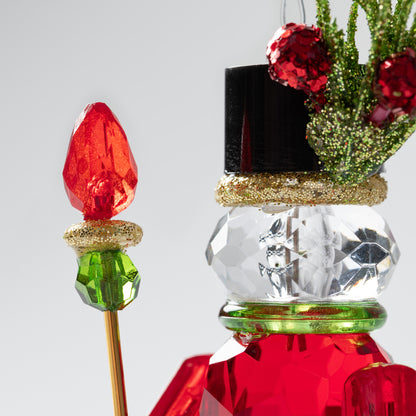 Decorative Christmas ornament resembling a nutcracker with red and green colors on a light gray background.