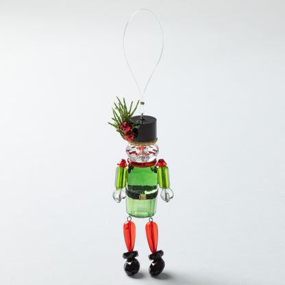 Decorative nutcracker ornament with green body, black shoes, and black top on a white background