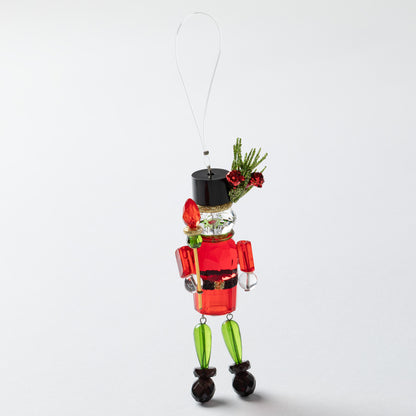 Decorative nutcracker ornament with red body, green legs, and black shoes on a white background