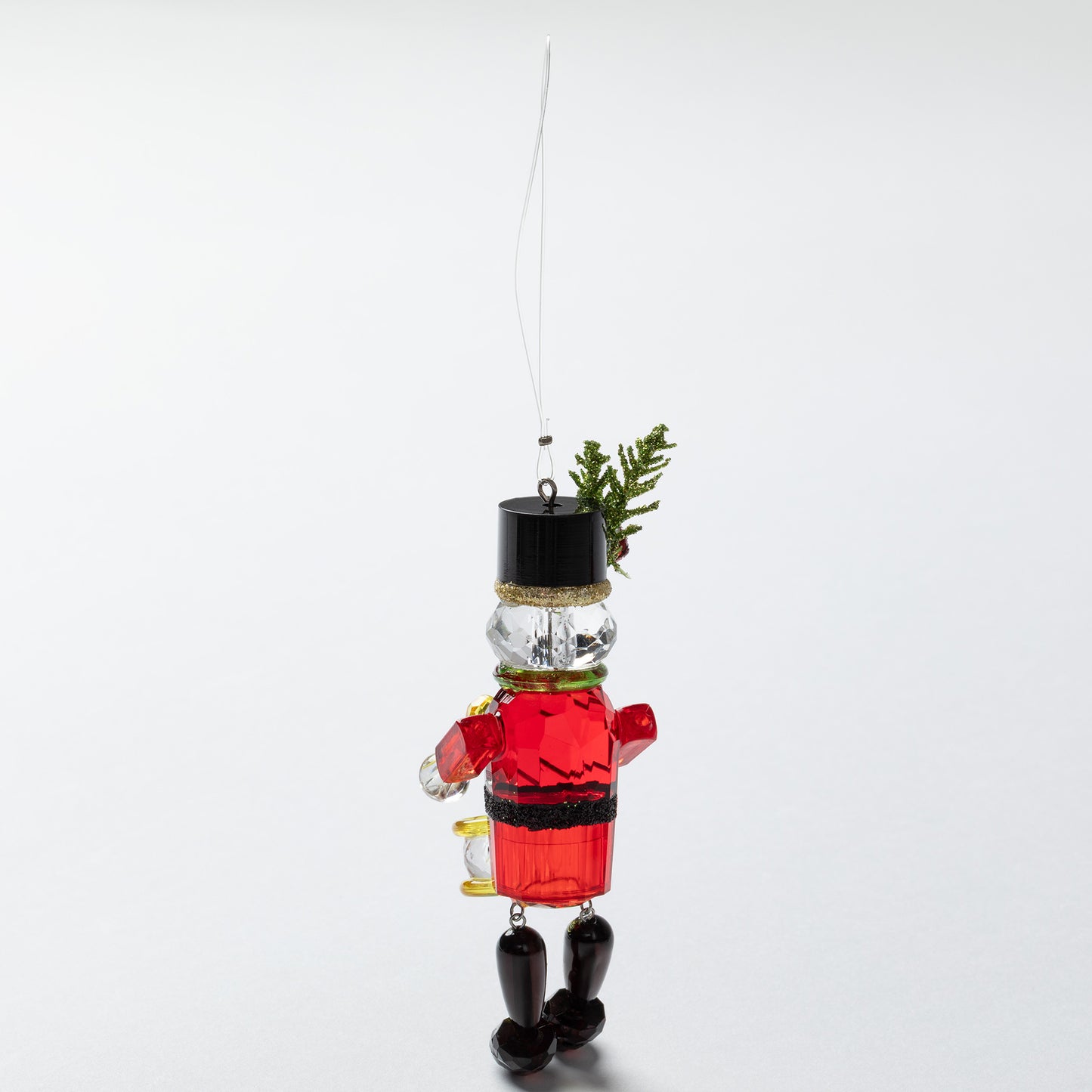 Decorative glass nutcracker ornament with a red outfit and black top hat on a white background