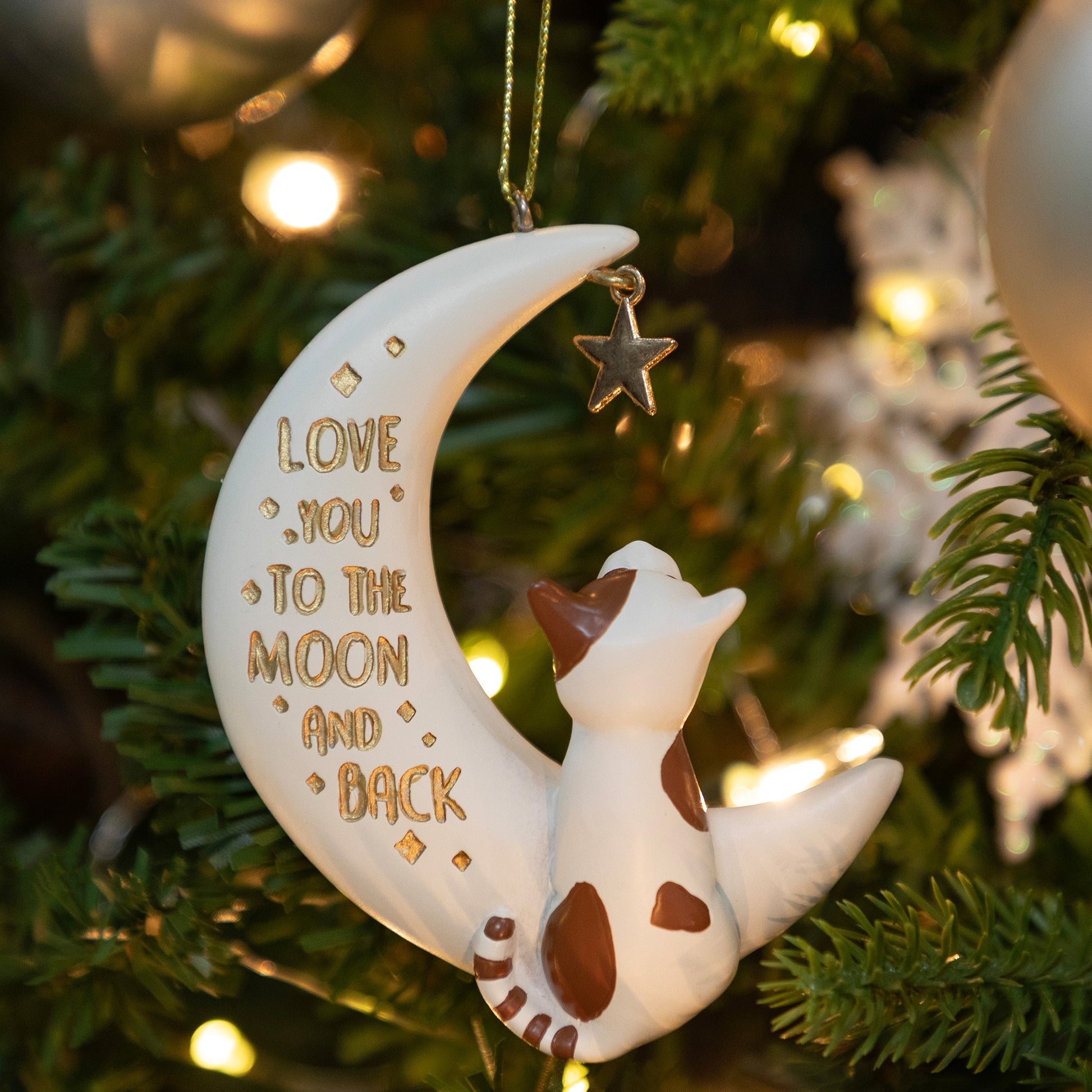 Decorative ornament with a cat on a moon, 'Love you to the moon and back' text, hanging on a Christmas tree.
