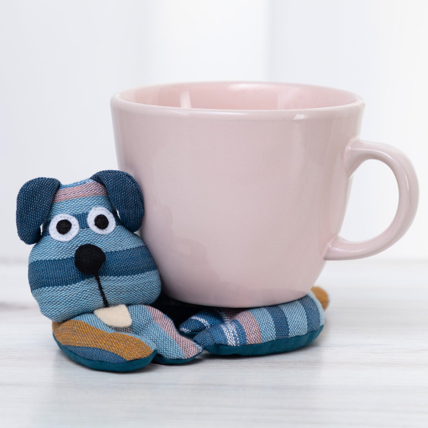 Striped dog-shaped coaster on a white background with a pink mug on top