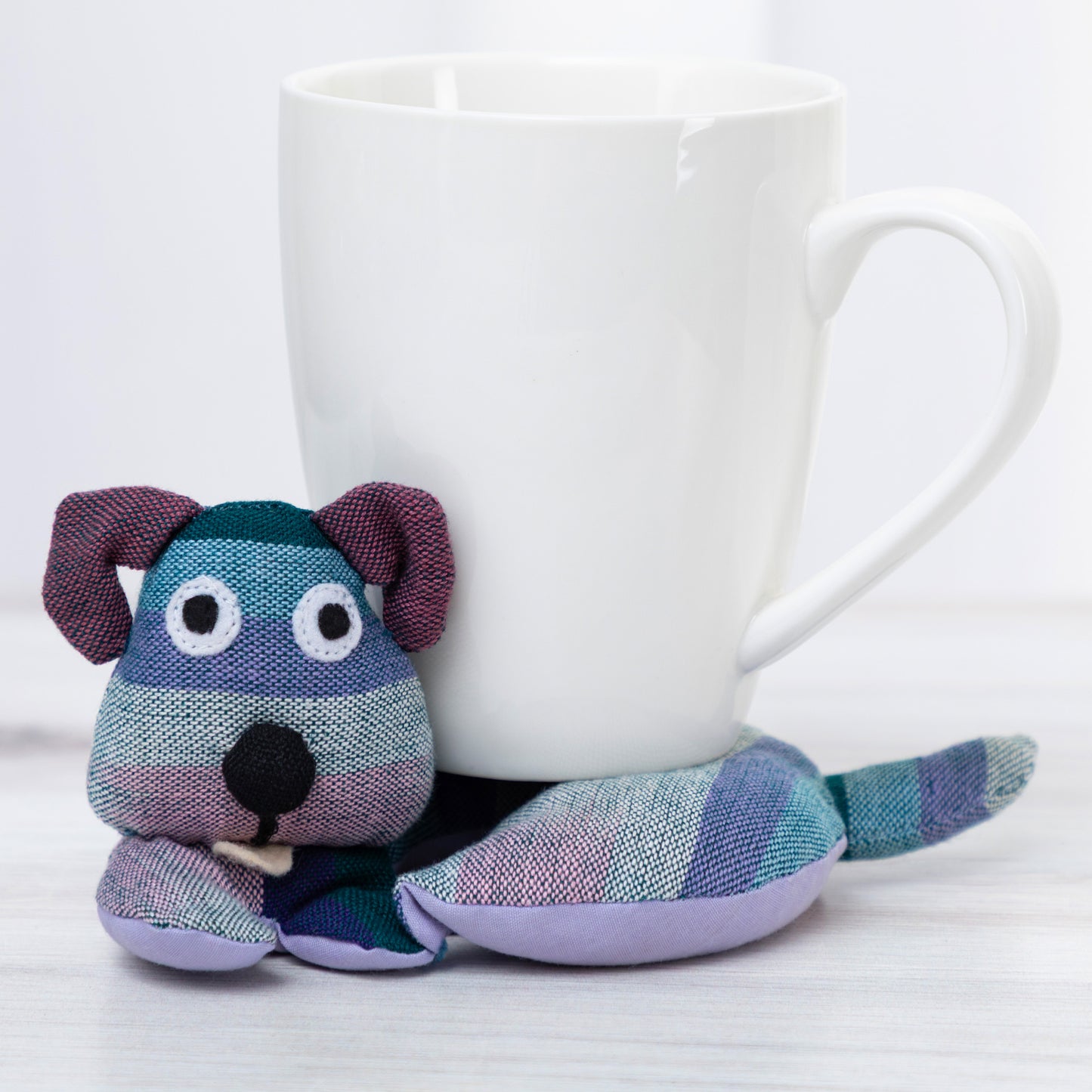 Plush dog-shaped mug cozy next to a white mug on a light background