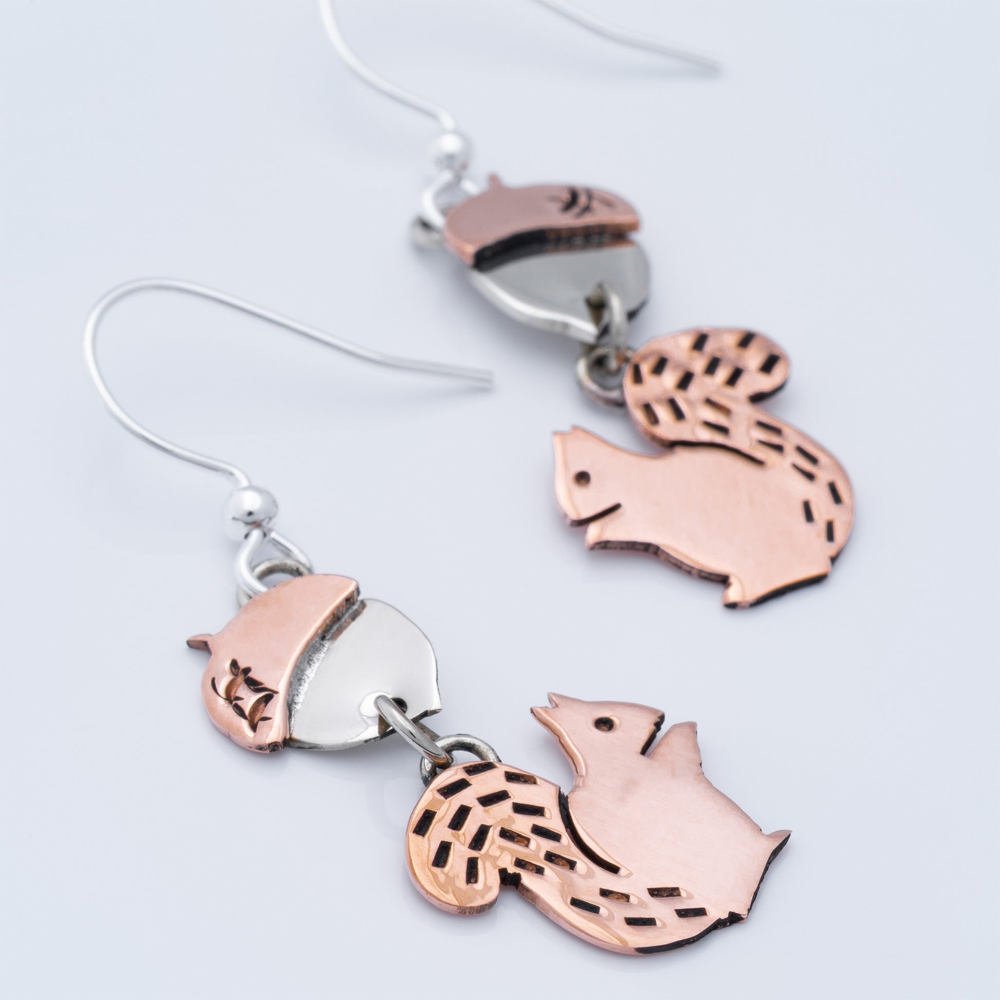 Pair of earrings with squirrel and acorn designs on a light gray background