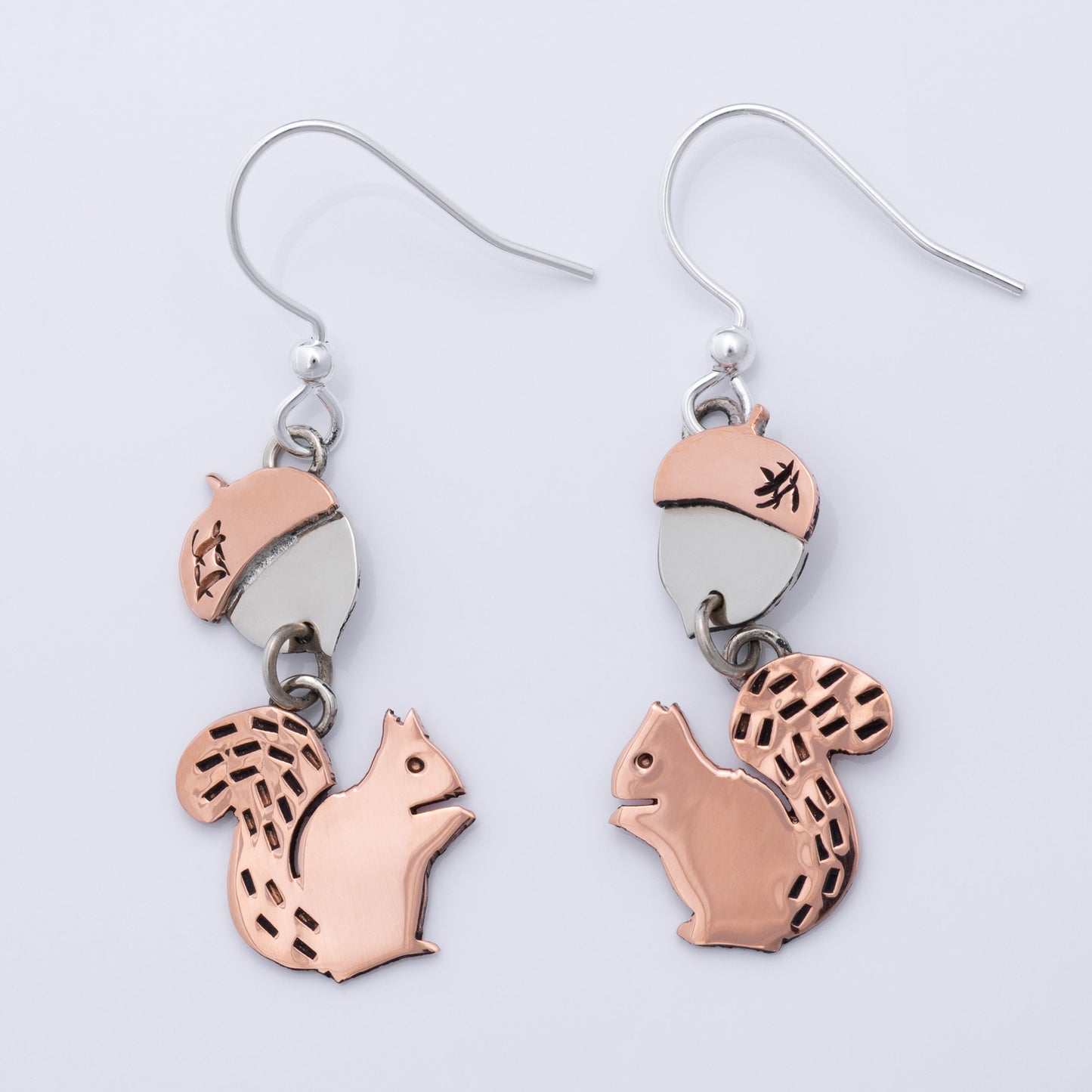 Squirrel-shaped earrings with copper and silver design on a light gray background