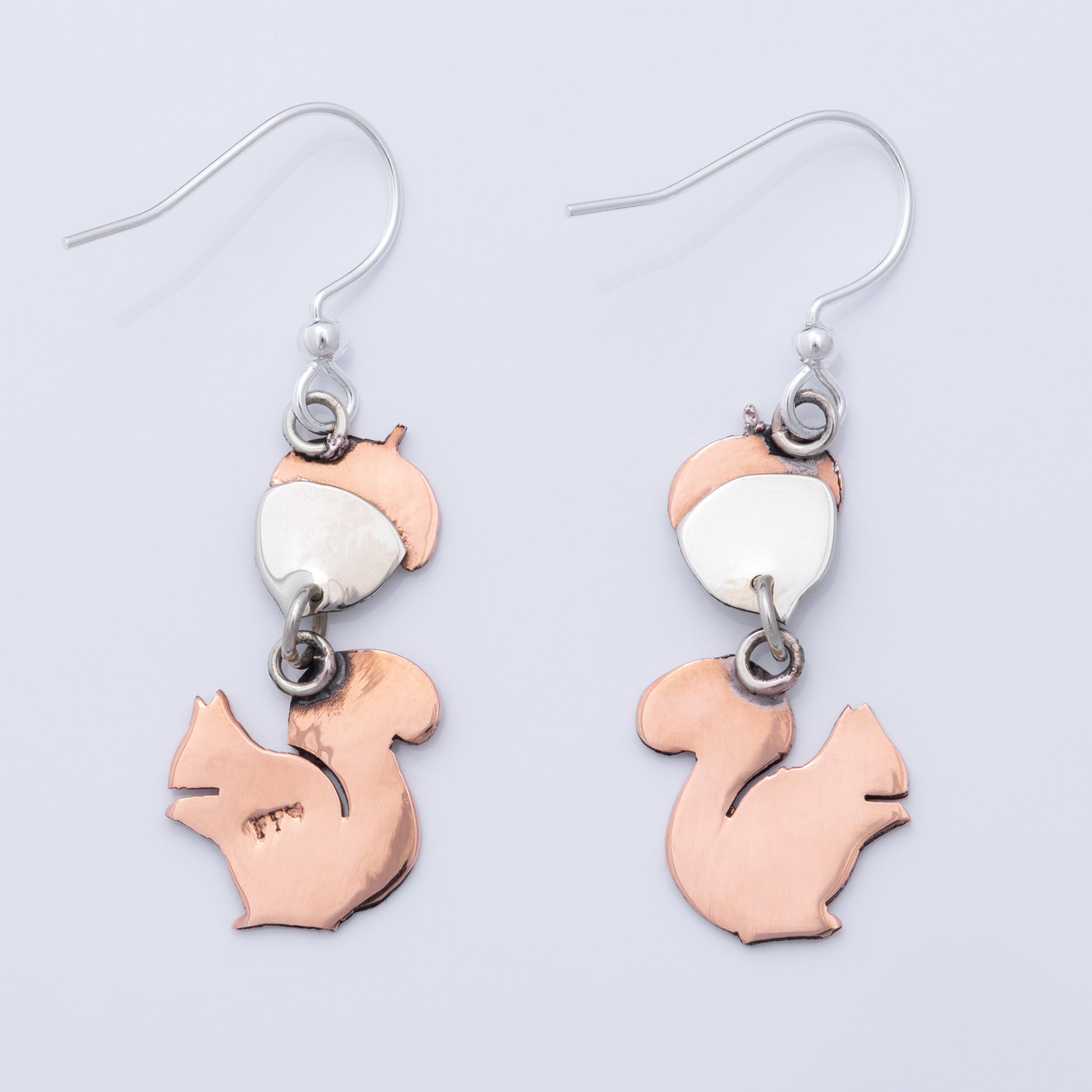 The backs of squirrel-shaped earrings with copper and silver design on a light gray background