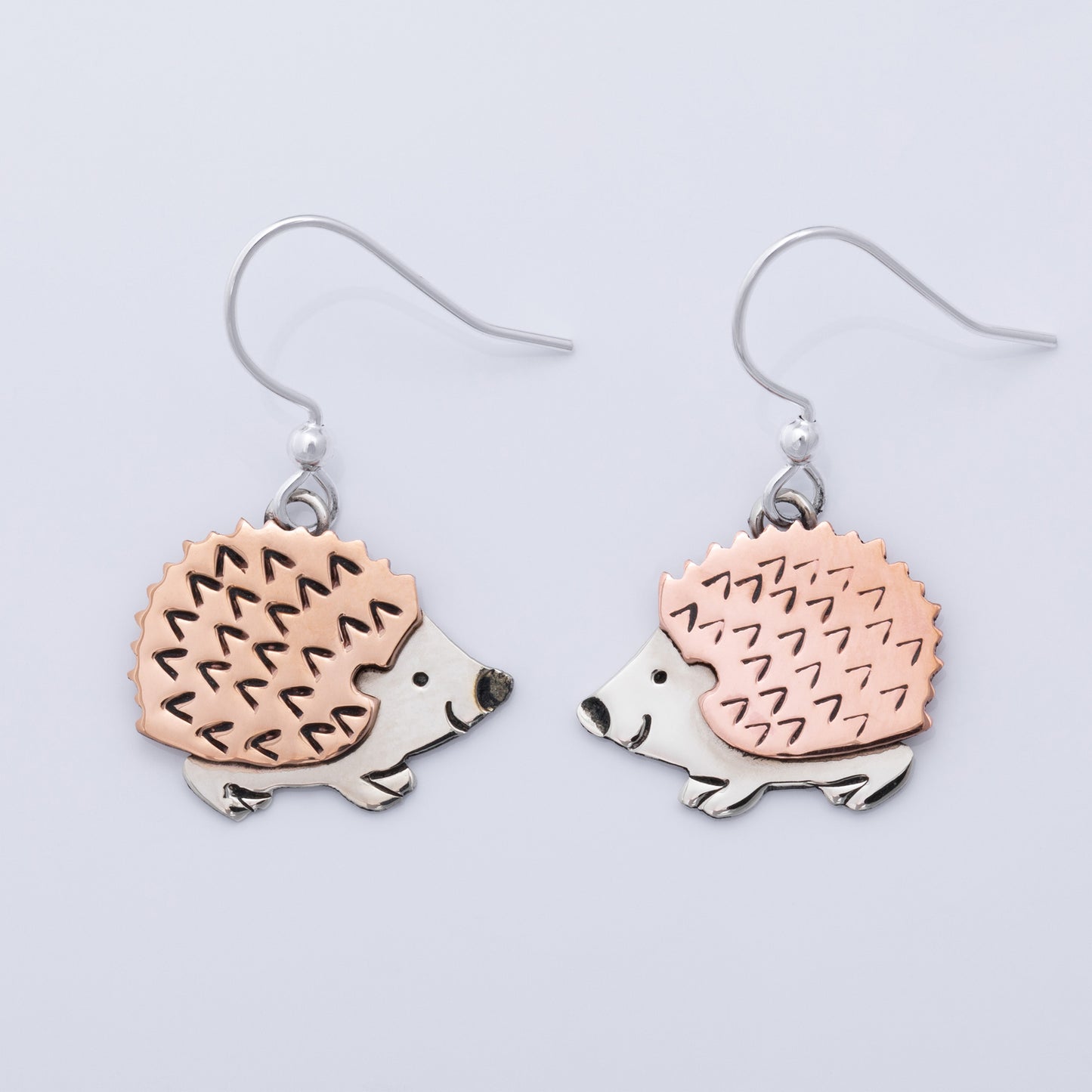 Hedgehog-shaped earrings with copper and silver design on a light gray background