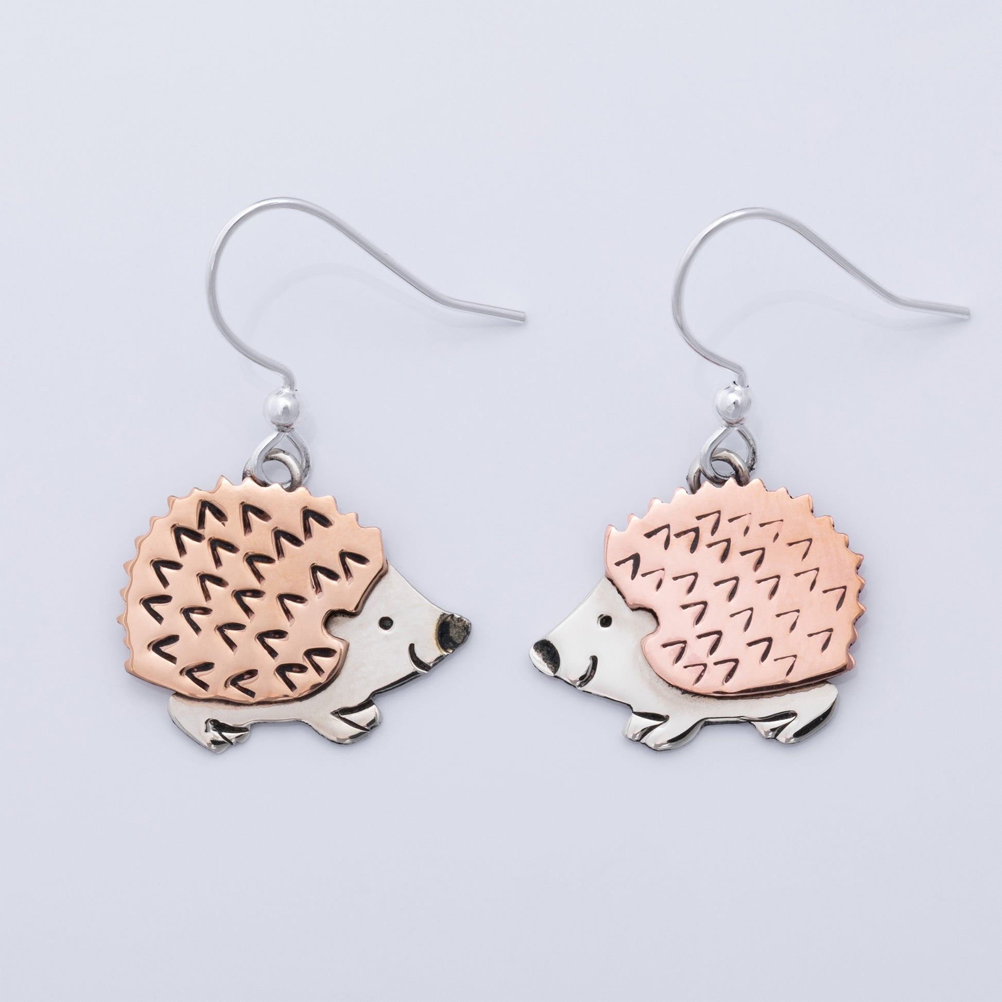 Hedgehog-shaped earrings with copper and silver design on a light gray background